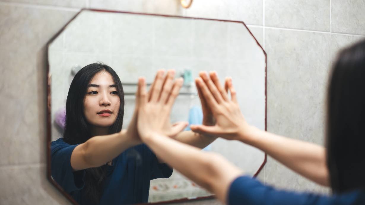 A woman pushing the image of herself in the mirror while dealing with negative self-talk.